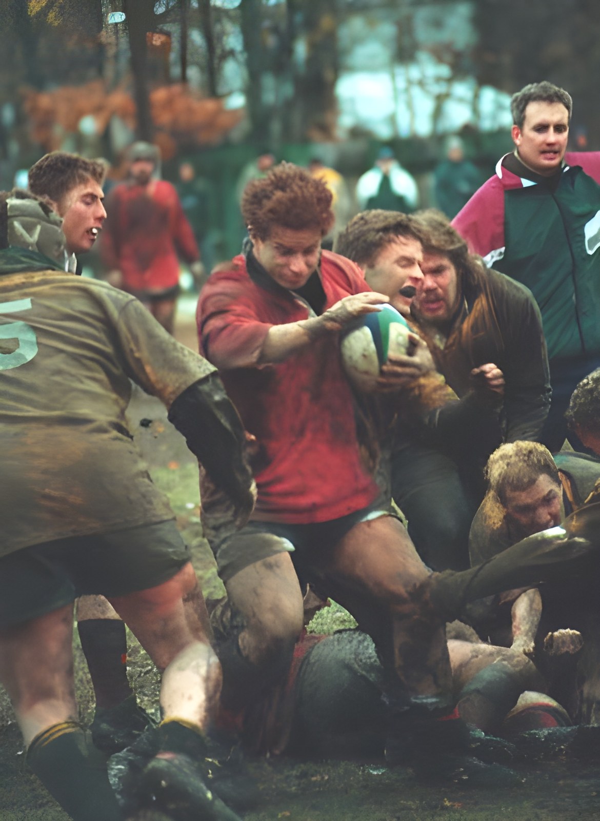 Nick Taylor in a red jersey carries the ball through a muddy ruck.
